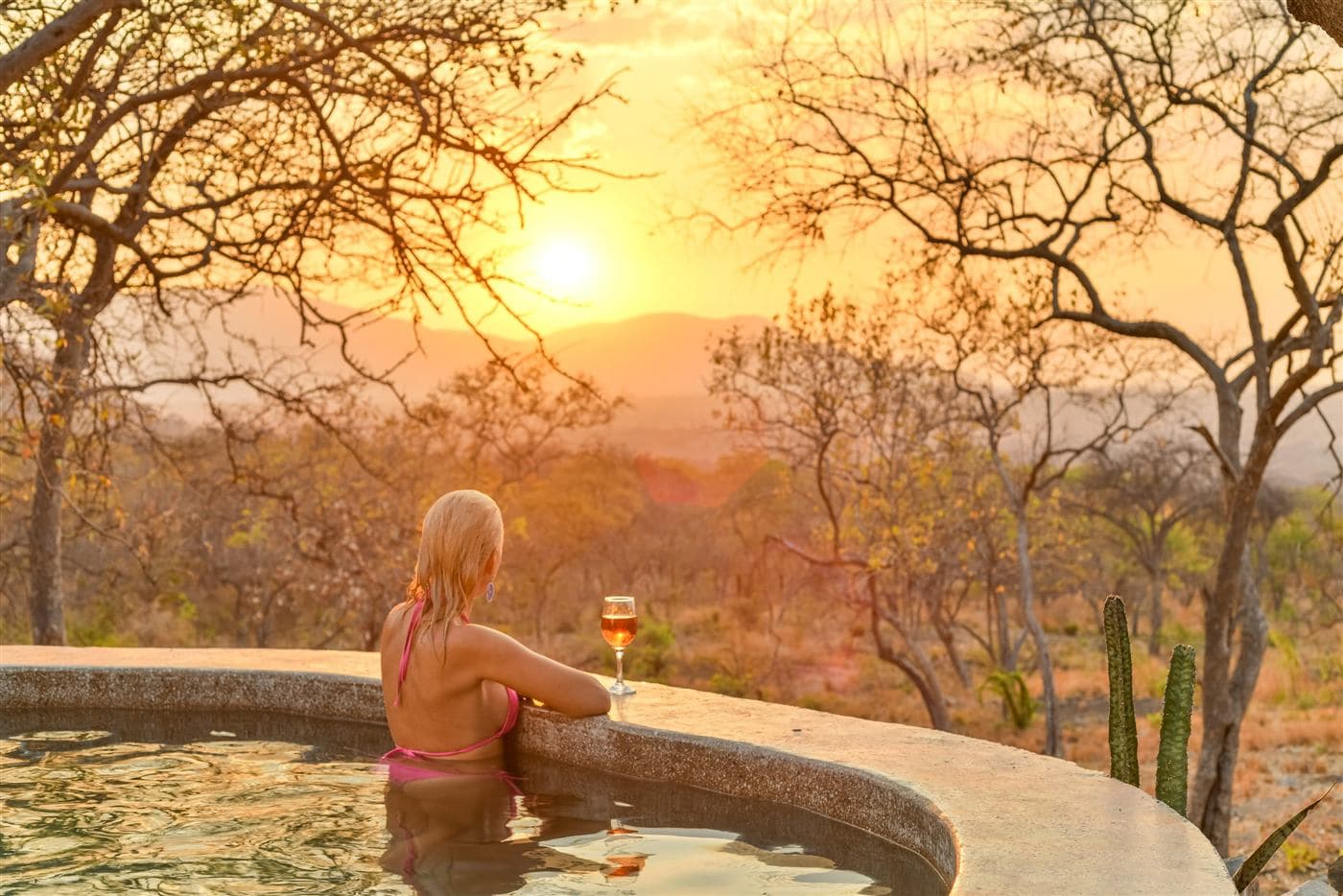 Guest in the infinity pool with wine at sunset